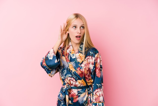 Young blonde woman wearing a kimono pajama trying to listening a gossip.