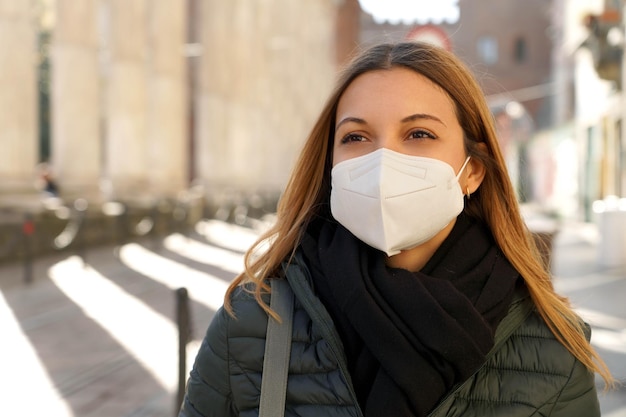 Young blonde woman wearing protective medical mask walking in the city with winter clothes