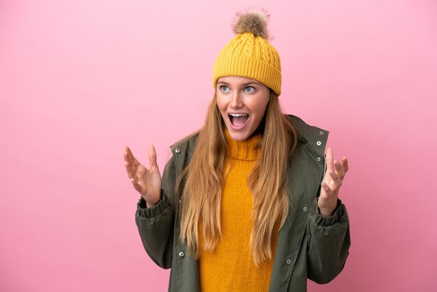 Young blonde woman wearing winter jacket isolated on pink background with surprise facial expression