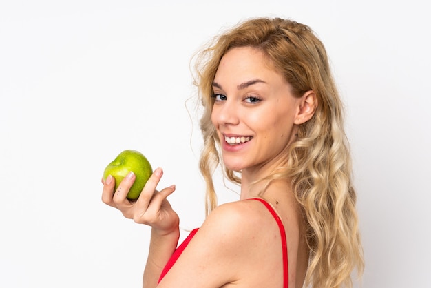 Young blonde woman on white eating an apple