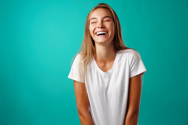 Young blonde woman in white shirt laughing with her eyes closed against mint