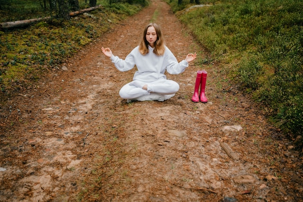 Young blonde woman in white tracksuit meditates in the forest