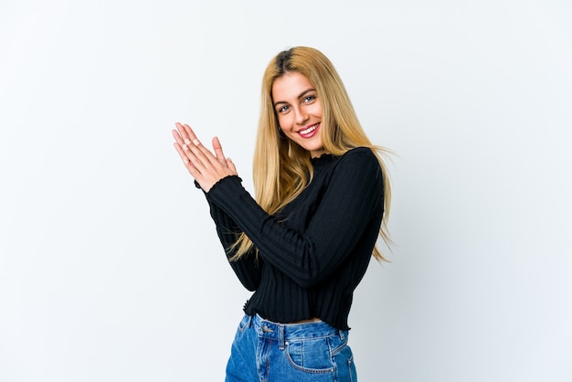 Young blonde woman on white wall feeling energetic and comfortable, rubbing hands confident.