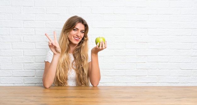 Young blonde woman with an apple making victory gesture