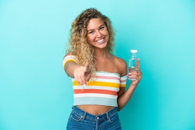 幸せな表情で正面を向いている青い背景に分離された水のボトルを持つ若いブロンドの女性