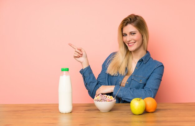 Giovane donna bionda con una ciotola di cereali che punta il dito verso il lato