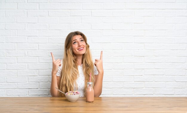 Young blonde woman with bowl of cereals pointing up