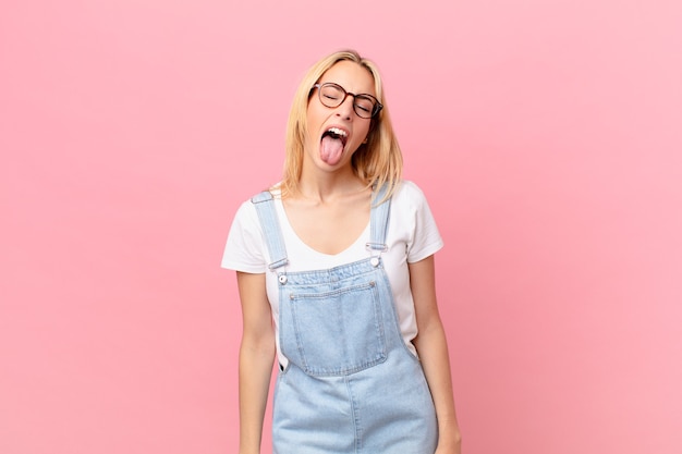 Young blonde woman with cheerful and rebellious attitude, joking and sticking tongue out