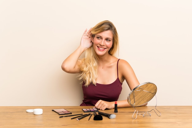 Young blonde woman with cosmetic in a table listening something