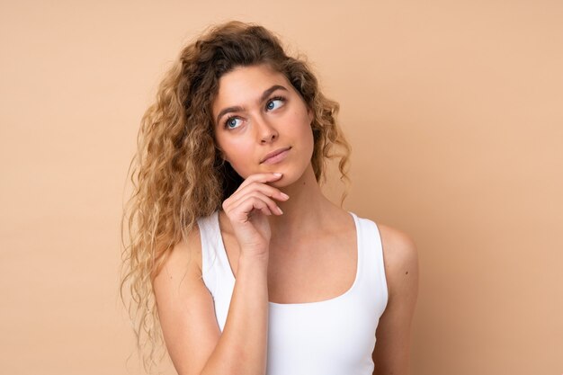 Young blonde woman with curly hair on beige wall