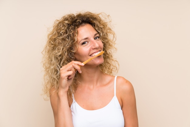 Young blonde woman with curly hair brushing her teeth