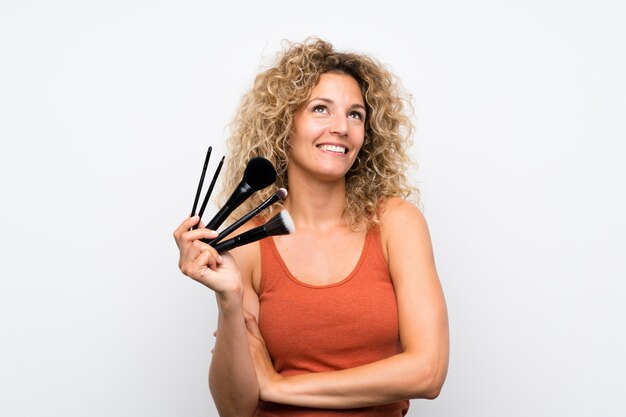 Giovane donna bionda con capelli ricci che tiene molta spazzola di trucco che cerca mentre sorridendo