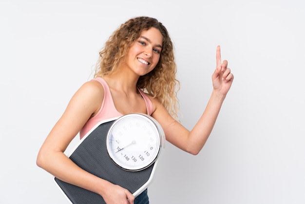 Young blonde woman with curly hair on white wall with weighing machine