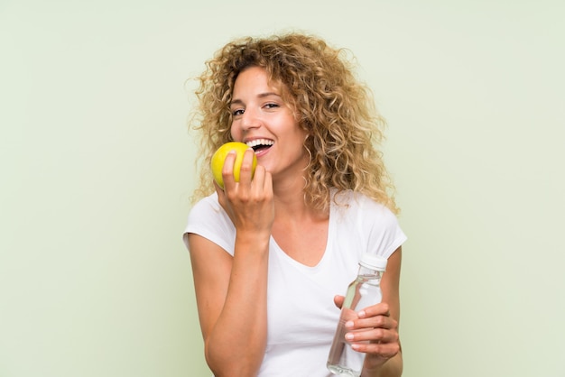 Young blonde woman with curly hair with an apple and with a bottle of water