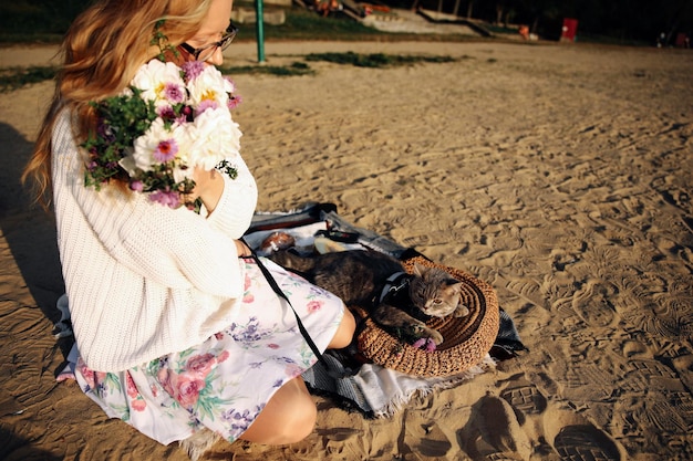 Young blonde woman with flowers on the beach with a pet Scottish Straight cat in the spring on a sunny day