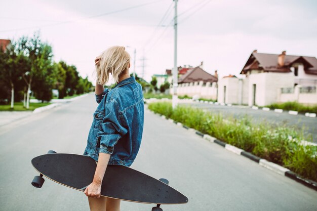 Young blonde woman with a longboard on street