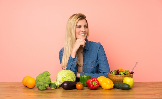 Young blonde woman with many vegetables looking to the side