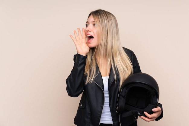 口を大きく開けて叫んで分離壁上のオートバイのヘルメットを持つ若いブロンドの女性