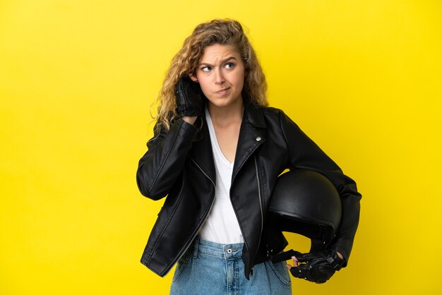 Young blonde woman with a motorcycle helmet isolated on yellow background frustrated and covering ears