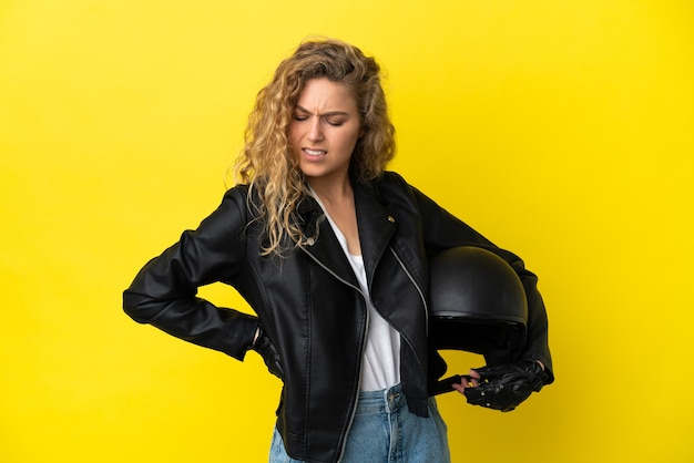 Foto giovane donna bionda con un casco da motociclista isolato su sfondo giallo che soffre di mal di schiena per aver fatto uno sforzo