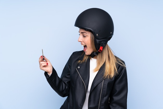 Young blonde woman with a motorcycle helmet and a key over isolated wall