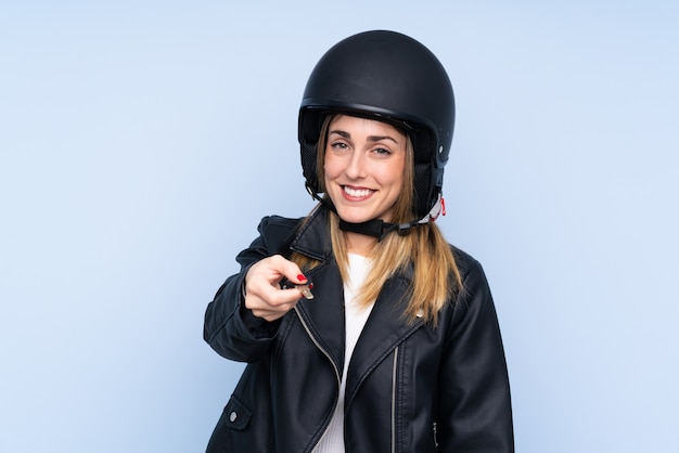 Young blonde woman with a motorcycle helmet and a key over isolated wall