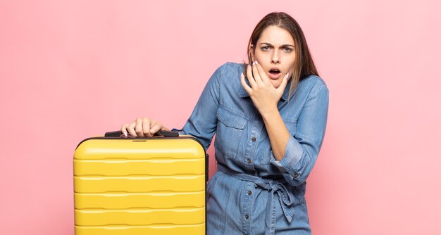 Young blonde woman with mouth and eyes wide open and hand on chin, feeling unpleasantly shocked, saying what or wow