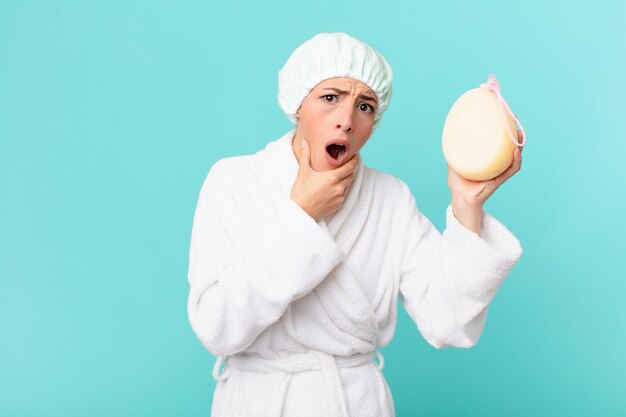 Young blonde woman with mouth and eyes wide open and hand on chin. shower concept.