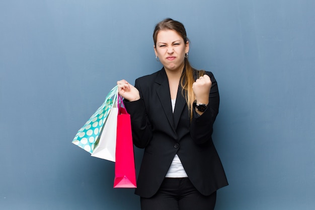 Young blonde woman with shopping bags against grunge wall