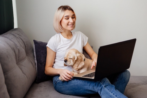 Giovane donna bionda con uno spaniel seduto a un laptop blogger che lavora su internet home office