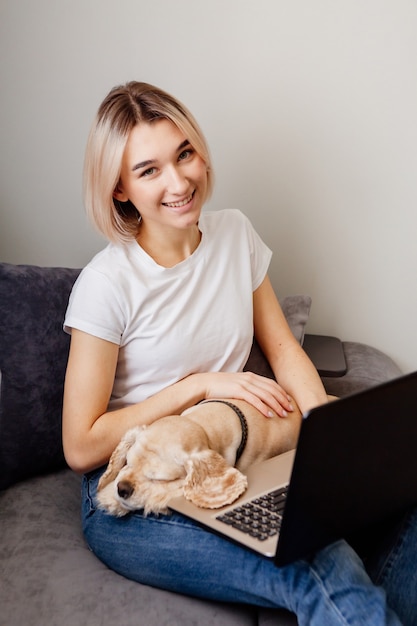 Giovane donna bionda con uno spaniel seduto a un laptop blogger che lavora su internet home office