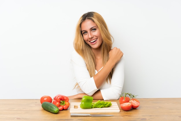 Young blonde woman with vegetables in a table celebrating a victory