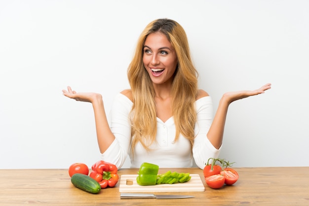 Young blonde woman with vegetables in a table with surprise facial expression