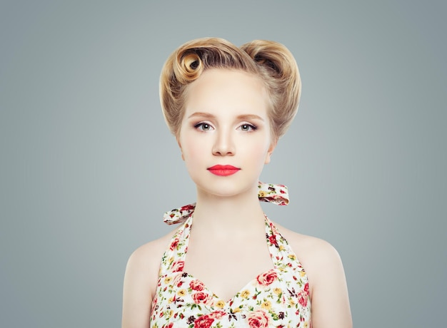 Young Blonde Woman with Vintage Retro Pinup Hairstyle and Makeup against Gray Wall Background