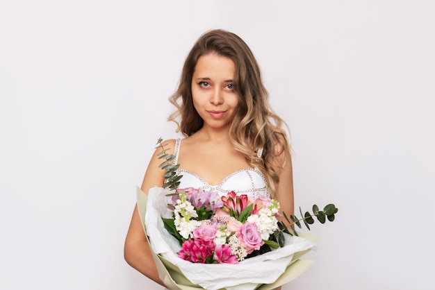 A young blonde woman with wavy hair holding a bouquet of flowers in a stylish package in her hands