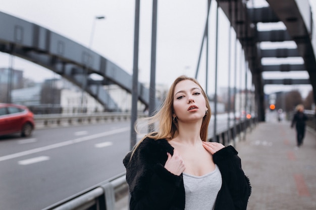 Young blondie business sensual woman near bridge. Walking along european city