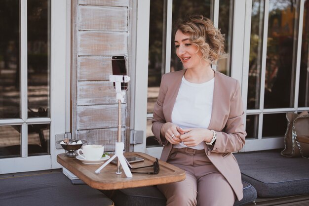 Young blondy woman blogger working in a street cafe on a mobile phone