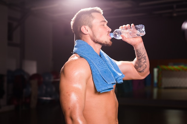 Young bodybuilder in the gym drinking a bottle water