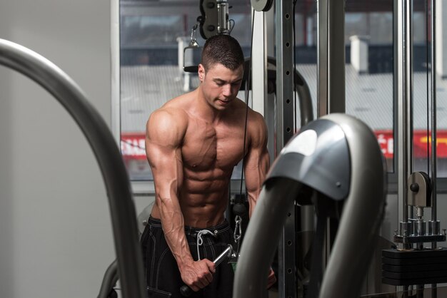 Photo young bodybuilder is working on his triceps with cable in a dark gym