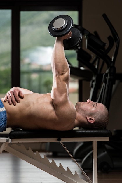 Foto il giovane bodybuilder sta lavorando sui suoi tricipiti con il manubrio in una palestra buia