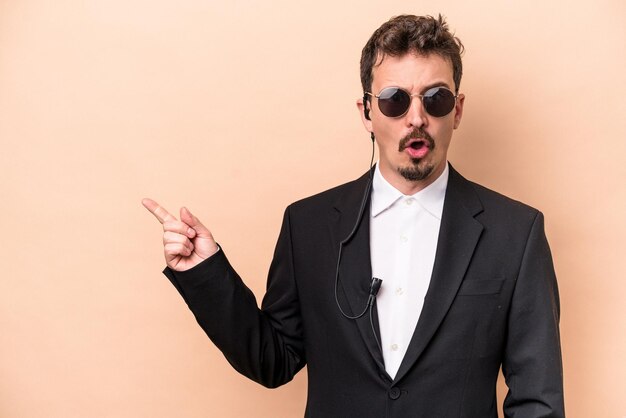 Young bodyguard caucasian man isolated on beige background pointing to the side