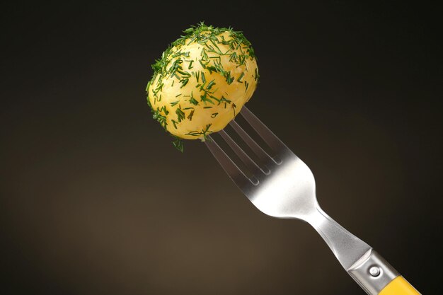 Photo young boiled potato on fork on dark background