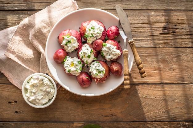 Young, boiled potatoes with sour cream and green onion on a wooden table