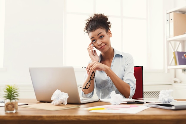Молодая скучно афро-американская женщина разговаривает по телефону в современном офисе с копией пространства. Бизнес-консультирование.