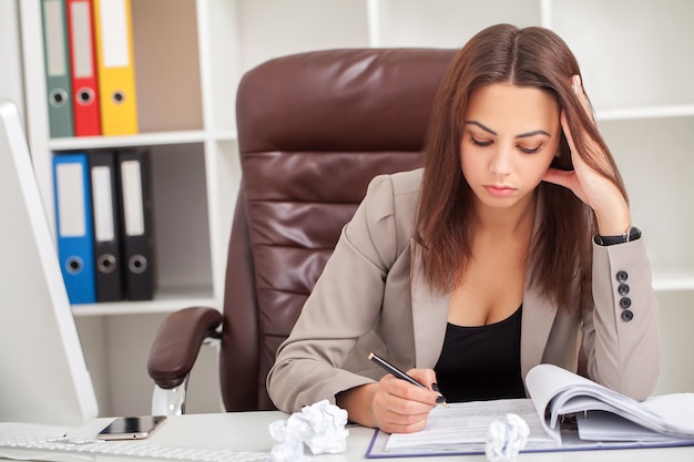 Young boring businesswoman sitting at the table with laptop and want to sleep while yawn at workplace in modern office.