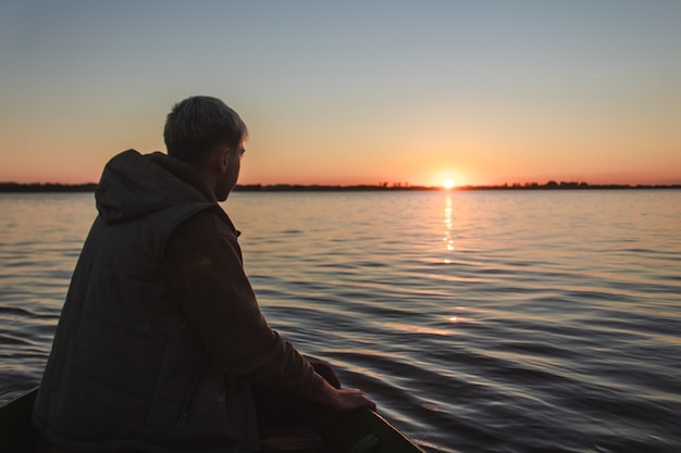 Мальчик оценивает закат с лодки в море.