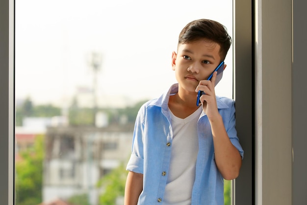 Foto un ragazzo, uno studente di una scuola elementare asiatica, tiene in mano uno smartphone che chiama e parla con qualcuno