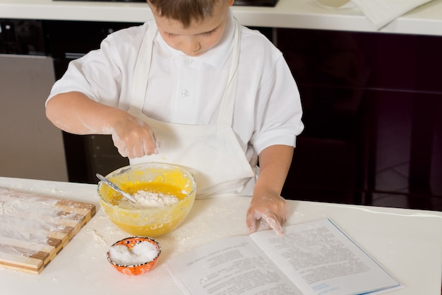 Ragazzo che cuoce aggiungendo farina all'impasto