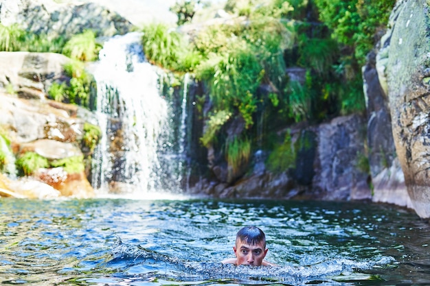 Young boy bathes in natural pool with waterfall.