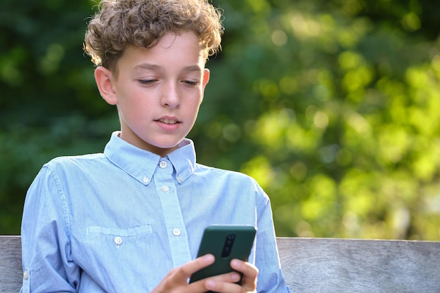 夏の公園で彼のスマートフォンを屋外で閲覧している少年レジャーと教育の概念のために携帯電話を使用して